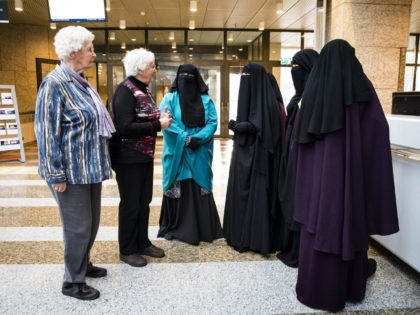 Two women stand next to women wearing niqab as they …