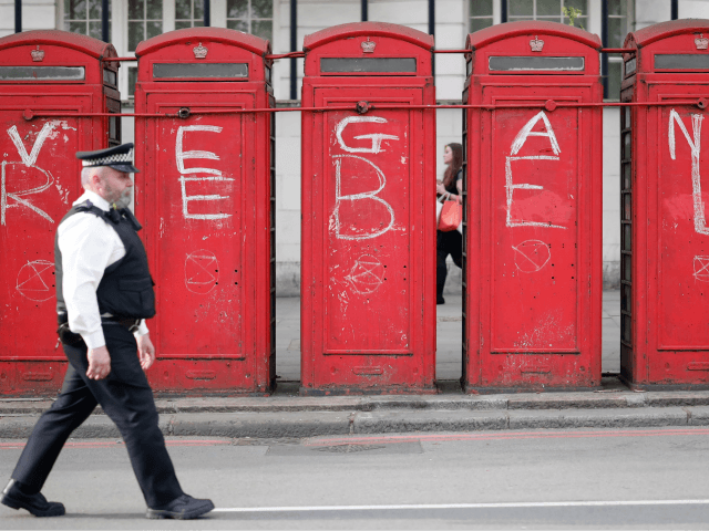 A police officer walks past public telephone boxes daubed with the words "vegan" and "rebe