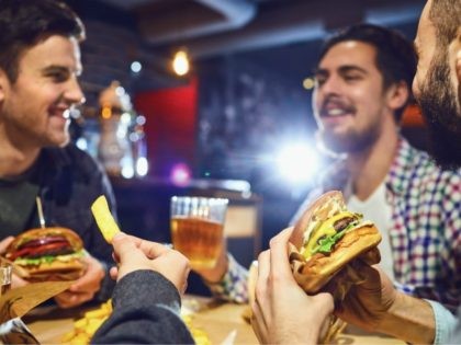 Happy friends eat burgers, drink beer in a bar. People in a fast food restaurant.