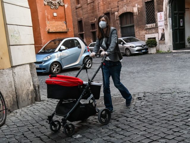 A woman wearing a face mask pushes a baby stroller in central Rome on April 15, 2020, duri