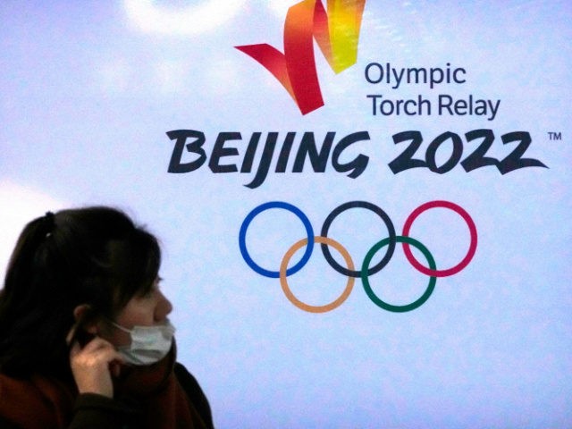 A woman wearing a face mask to protect against COVID-19 walks past the logo for the Beijin