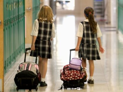 Eight year old girls head home after after school rolling their backpacks down the school
