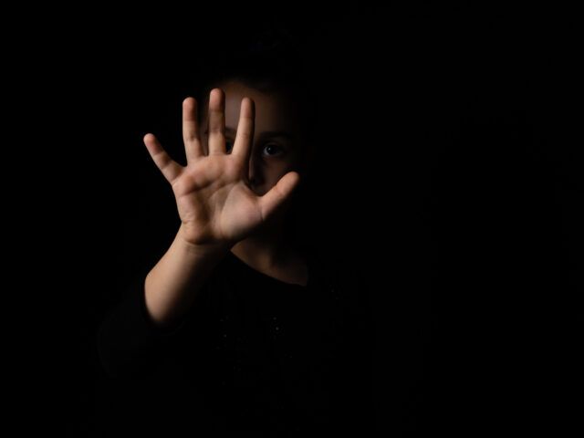 little girl with a raised hand making a stop sign gesture on a black background. harassmen
