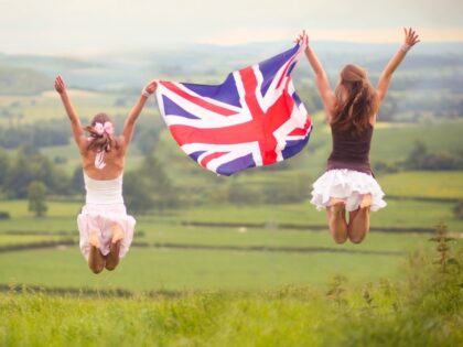 British Countryside in background, two girls flying union jack flag, Dorset, UK.