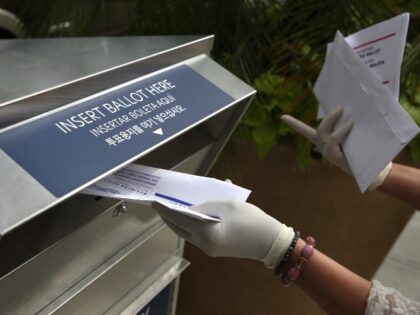 FILE - A woman wearing gloves drops off a mail-in ballot at a drop box in Hackensack, N.J.